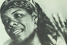 Black-and-white photograph of a African American woman in her forties, wearing a bandana and raising her left hand.