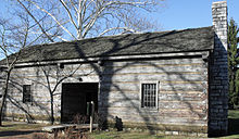 A log structure with a central breezeway with windows on either side and a chimney on the right
