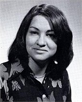 A formal pose of a young woman in her early twenties, dark straight hair parted near the center, wearing a dark floral print top.