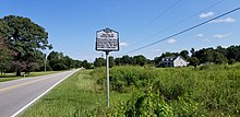 A picture of a highway marker in a rural area reading "Battle of Hayes Pond: The Lumbee and other American Indians ousted the Ku Klux Klan from Maxton. Jan. 18, 1958, at rally half a mile west"