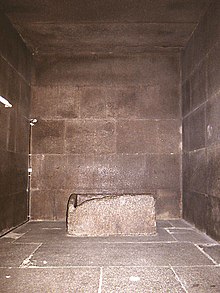 Square chamber constructed out of red granite blocks with a granite sarcophagus in the center.