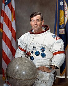 Official photograph of Young in an Apollo spacesuit with a globe of the Moon