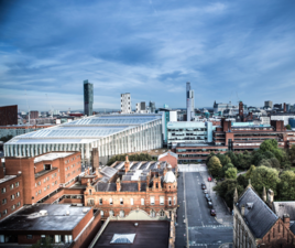 The image shows the Manchester Metropolitan University Business School, the All Saints campus and the Manchester skyline.