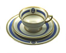 An elegant drinking cup on a saucer. Both are in white ceramic with pale blue and gold decoration.