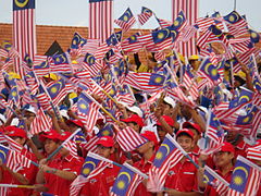 A large crowd of boys in red shirts and caps waving Malaysian flags