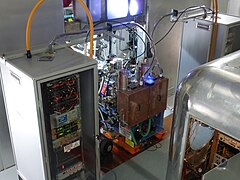 Two ion sources at the center with two high-voltage electronics cabinets next to them[25]