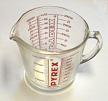A clear glass measuring jug featuring red markings and text.
