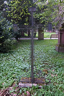 Fotografie eines filigran gearbeiteten Eisernen Grabkreuzes auf einer überwucherten Wiese.