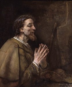 Painting of a bearded man in brown robes praying next to a brown wall.