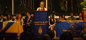 Picture of speaker making speech, with others on podium, with words "Phi Theta Kappa" on banner