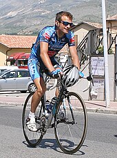 A cyclist riding while holding his helmet
