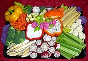 Brightly colored veggie platter arranged over purple cabbage with "rosebud radishes" and sweet peppers used as serving containers