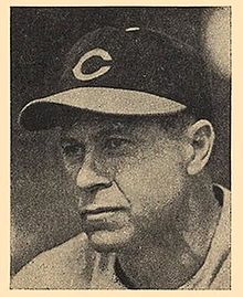 A black and white photograph of a man wearing a baseball cap with a "C" on the front
