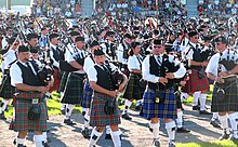 A hundred or more pipers and drummers in an array of kilts at a Scottish games event