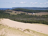 People on sandy dunes overlooking farmland and the lake