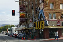brick casino with hints of art deco style. A faded sign on the corner is a prospector with a pick axe with the words "Nevada Club" next to a vintage mechanical slot machine.