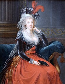 A woman bedecked in pearls wears a blue and red dress.