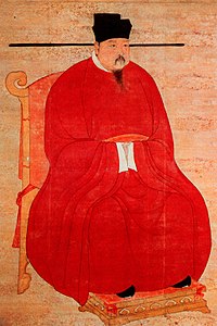 A portrait-oriented scroll depicting a man in thick red robes, black pointed shoes, and a bucket-shaped black hat with long, thin protrusions coming out horizontally from the bottom of the hat, sitting on a throne.