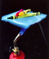 An aerogel holding crayons, with a flame lit underneath, demonstrating its excellent insulation from heat. (NASA)