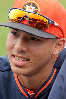 A closeup of the face of man with sunglasses on the bill of an orange baseball cap.
