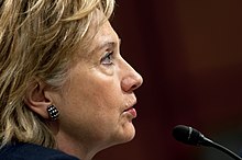 Side profile of Clinton facing toward her right side. She is speaking into a microphone.