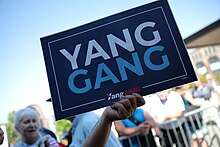 A blue yard sign with white and red letters spelling out 'Yang Gang'