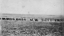 A line of men on horses charge across an open field towards the camera.