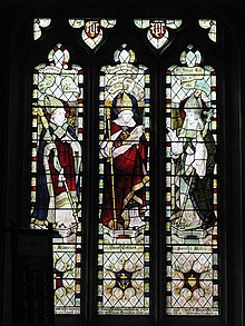 Three stained glass windows, each depicting a mitred and robed figure. All three are carrying staves.
