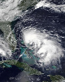 A visible satellite image of Tropical Storm Humberto northeast of the Bahamas and east of Florida. Cuba is visible near the bottom of the frame. The storm's cloud pattern is asymmetric, with most thunderstorm activity north of the center.