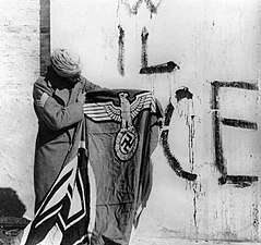 Indian soldier holds captured swastika flag after surrender of German forces in Italy