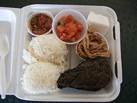 Traditional Hawaiian plate lunch. Clockwise, from bottom left: two scoops of white rice, ahi poke, lomi-lomi salmon, haupia dessert, kālua puaʻa (roast pork), and pork laulau.