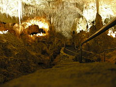 A picture of a partially illuminated cave with a jagged rock ceiling and a walkway extended into the cavern.