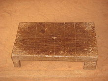 rectangular wooden stool with lines etched into the surface in four rows