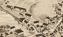 A cropped portion of a bird's-eye-view map. It shows a rail line ending in a small village. A station building and several rail yard buildings are shown.