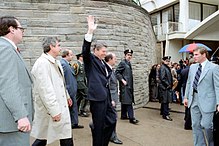 Ronald Reagan waves his hand as he walks out of the Washington Hilton. Surrounding him are secret service agents, policemen, press secretary James Brady, and aide Michael Deaver.