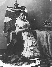 Photograph of Queen Kapiʻolani seated on a chair with her crown on a table to the right