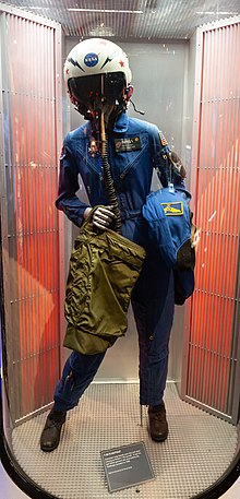 A mannequin wears her flight helmet with mask as well as the flight suit.
