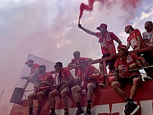Monza players on an open top bus. A player is holding a red flare.