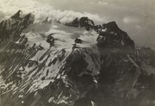 Old photo of a mountain in the clouds with a white glacier at the foot of the peaks.