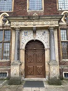 A photograph of the wooden front door of the house, surrounded by early 17C architectural embellishments such as columns and carvings