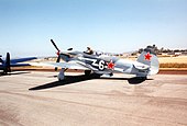 Propeller fighter on tarmac with pilot standing up in open cockpit. Red star