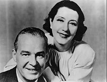 middle-aged white couple smiling at the camera, she leaning over his shoulder