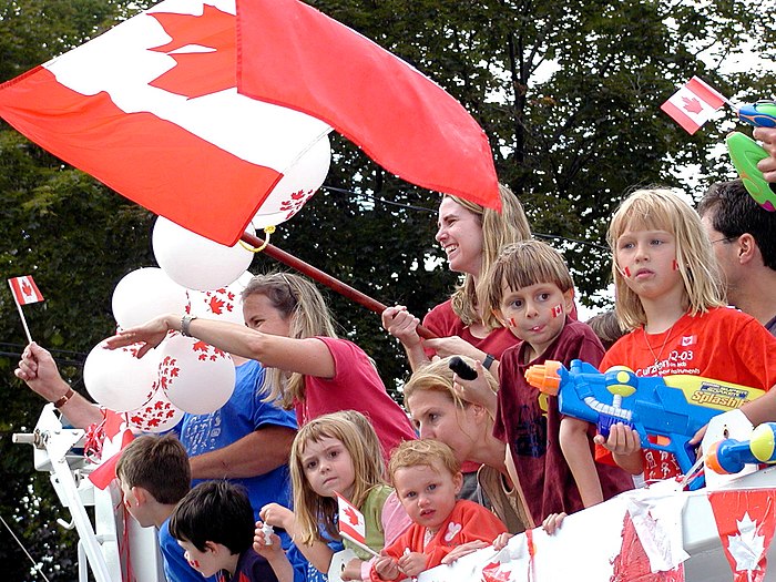 Photograph of children at a parade with a woman waving a Canadian flag