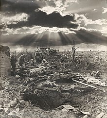 A photograph of a muddy shattered landscape with a concrete blockhouse and men lying on the ground
