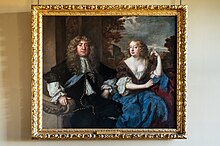 A finely dressed middle-aged couple shown sitting in a classical landscape. He wears courtly dress and a long wig, while she wears a low-cut gown and long wavy hair flowing down her back.