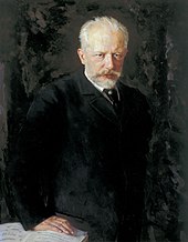 A middle-aged man with grey hair and a beard, wearing a dark suit and staring intently at the viewer.