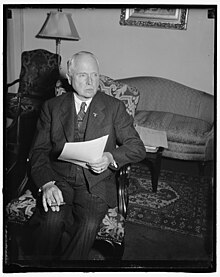 Charles Edward seated in a domestic setting wearing a suit