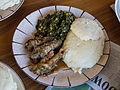 A meal of sadza (right), greens, and goat offal. The goat's small intestines are wrapped around small pieces of large intestines before cooking.