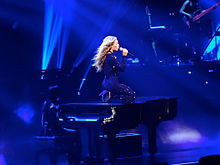 A woman kneeling upon a piano whilst singing