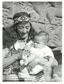 Guide Rangi, probably middle-aged, looking down at a baby in her arms and smiling